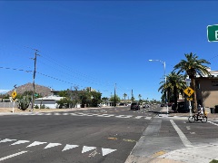 Sunny intersection with palm trees, cars, pedestrian signs, and a mountain in the background.