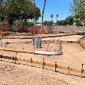 Construction site with concrete forms for pathways and planters, with trees and surrounding buildings.