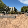 Pathway under construction with concrete forms for planters and an accessible ramp, surrounded by trees.