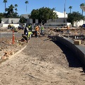 Continuation of pathway construction to City Hall with workers, construction materials, and trees.