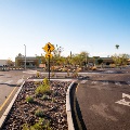 Pedestrian crossing sign at roundabout with clear blue sky and buildings.