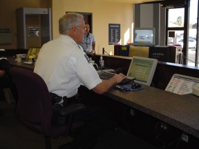 Security officer works on computer in lobby with someone in background.