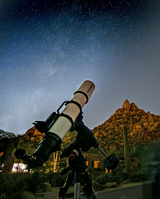 Telescope pointed at a starry sky near Pinnacle Peak with illuminated rock formations in the background